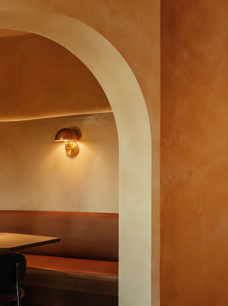 A glowing brass sconce inside a curved plaster archway